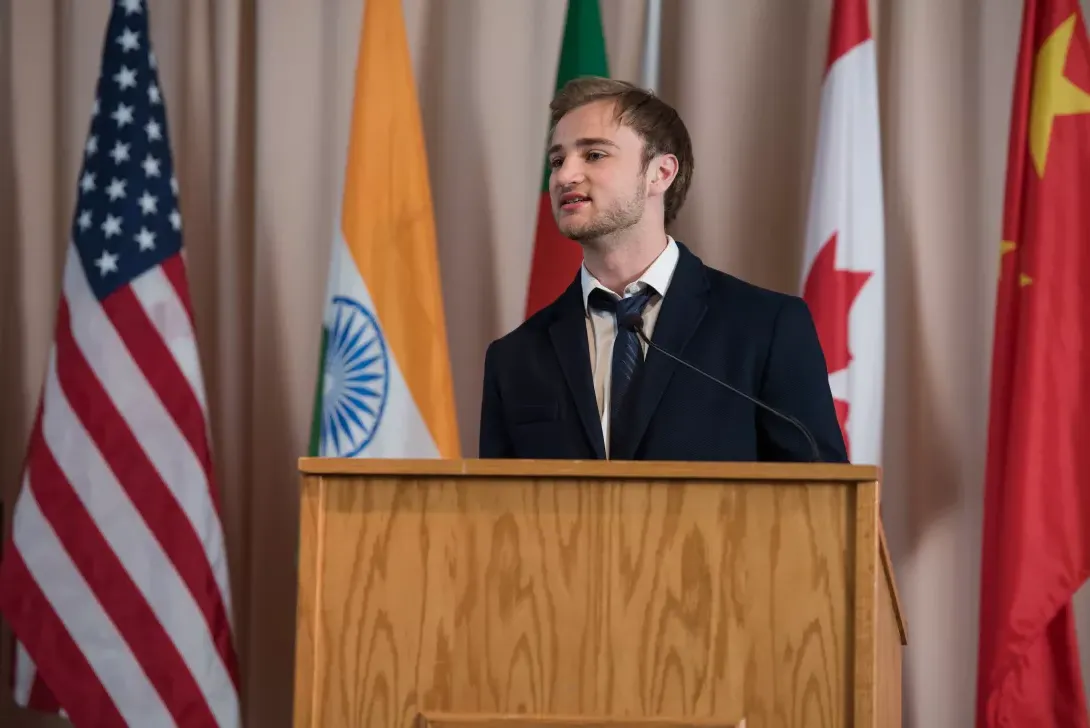 International student speaking at podium with flags from various countries in background